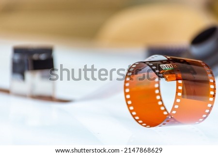 Rolls of film with a section of unrolled film showing individual frames on a  light table with equipment in the background. Selective focus.