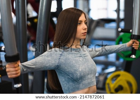 Close-up of a fit girl who exercises on a butterfly machine Royalty-Free Stock Photo #2147872061