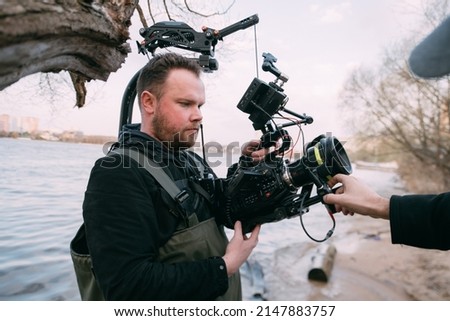 Director of photography with a camera in his hands on the set. Professional videographer at work on filming a movie, commercial or TV series. The filming process on the street, on location