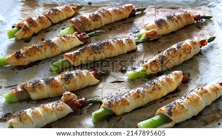 Freshly oven baked asparagus wrapped in prosciutto and puff pastry, decorated with poppies seeds on wooden background. Spring season. Directly above.