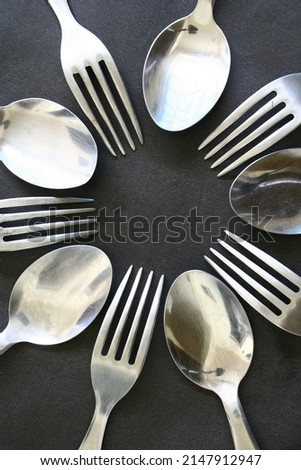 Circle of stainless steel spoons and forks for ways to eat, with light from height present an illustration of glitters and abstract shapes with a dark background