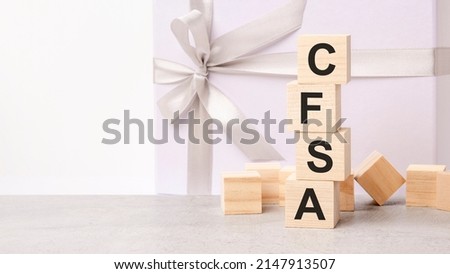 the CFSA text is laid out in a pyramid of wooden cubes. in the background is a paper gift box with a shiny white ribbon. CFSA - short for Certified Financial Services Auditor