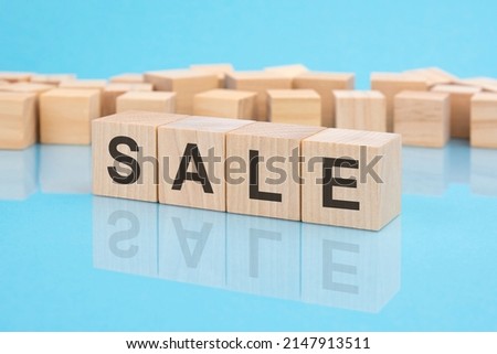 sale - word written on wooden blocks. text is written in black letters and is reflected in the mirror surface of the table, blue background