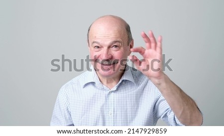 Senior caucasian bald man with mustache showing something small with figers.