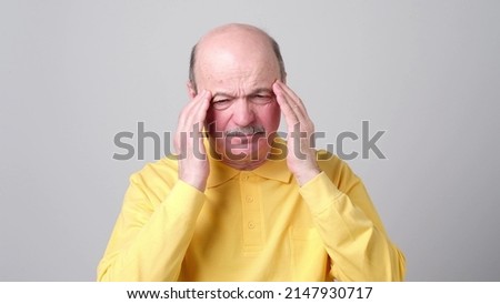 Mature man in yellow tshirt with closed eyes touching his head in pain. Health problems at old age, neuralgia concept Royalty-Free Stock Photo #2147930717