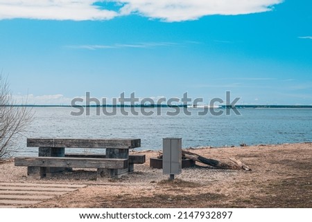 A cozy place for a picnic in the summer near a pond - a wooden table, benches and a trash can, near a fire pit, Latvia.