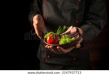 Preparation of beef steak and fresh vegetables. Plate with food in the chef hand. Dark background free space for advertising. European cuisine