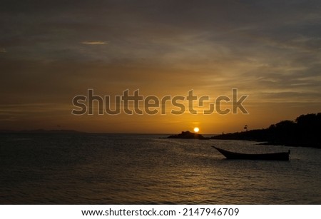Spectacular sunset colorful with red and orange in the coast of Margarita island There is a boat and mountain far away Picture taken in Juan Griego bay, at Margarita island Venezuela