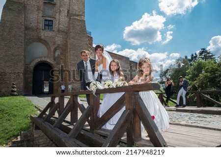 The groom, the bride and two little girls against the backdrop of the tower of the old castle.