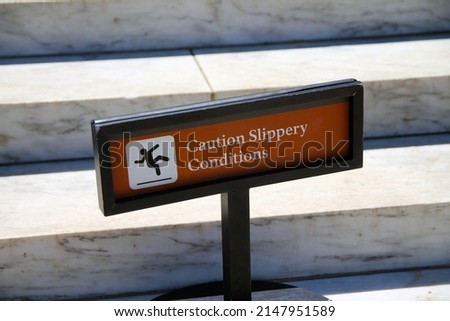 Caution, slippery conditions brown sign with icon representation on marble steps with a black holder on a sunny day