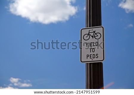 Yield to Peds sign hanging on a black pole with the sky and the clouds on the back, with bicycle icon