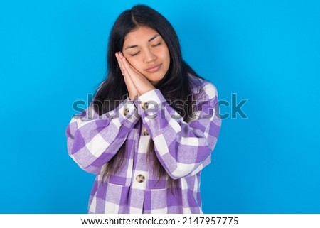 young hispanic woman wearing plaid shirt over blue background sleeping tired dreaming and posing with hands together while smiling with closed eyes.
