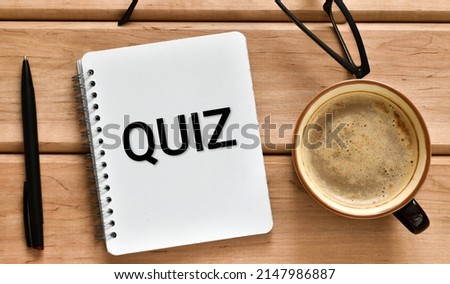 On a wooden office table is a notebook with the text QUIZ and cup of coffee, pen and eyeglasses. Business concept.