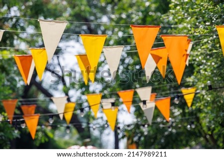 white, yellow and orange triangle flags hang on white rope in garden view. concept : fun party. Royalty-Free Stock Photo #2147989211