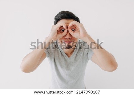 Funny obvious peeking Asian man in grey t-shirt isolated on white background.