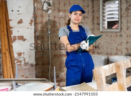 Portrait of young female foreman making notes while examining interior space of building before renovation