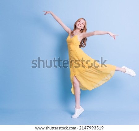 Full length image of young Asian woman wearing yellow dress on blue background Royalty-Free Stock Photo #2147993519