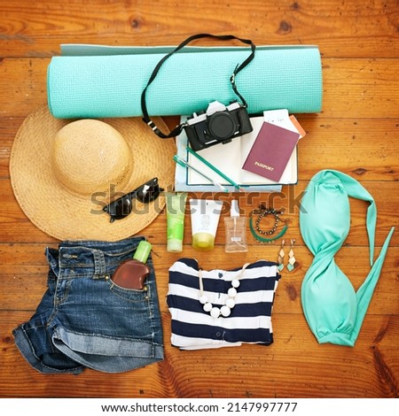 Planning for a perfect beach day. High angle shot of beachwear and travel paraphernalia arranged on a wooden floor.