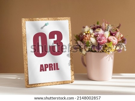 April 3. 3th day of month, calendar date.Bouquet of dead wood in pink mug on desktop.Cork board with calendar sheet on white-beige background. Concept of day of year, time planner, spring month.