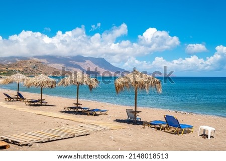 View to sun loungers and straw parasols on a beach. Kissamos, Crete, Greece Royalty-Free Stock Photo #2148018513
