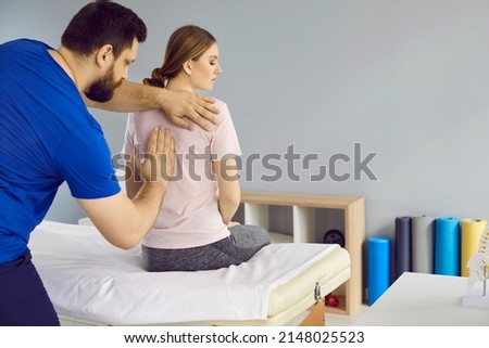 Osteopathic medicine and physiotherapy. Professional chiropractor treats young woman's back pain in modern medical clinic. Male doctor fixes back muscles in woman sitting on couch in hospital room. Royalty-Free Stock Photo #2148025523