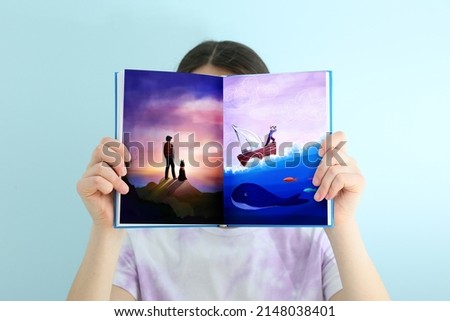 Little girl holding open book with drawn seascape against light background