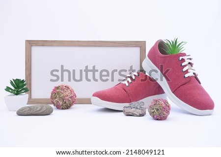 A pair of burgundy shoes in a shop window. There is a frame with space for text. The concept of environmentally friendly shoes. Shoes made from recycled materials. Nature design elements: grass