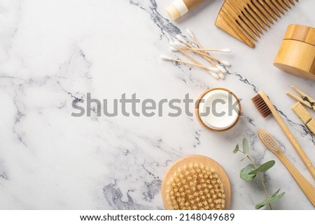 Top view photo of anti-cellulite washcloth wooden bottles bamboo hairbrush cream jar toothbrushes cotton buds clothespins and eucalyptus on white marble background with copyspace