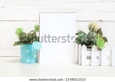 Party invitation mockup on a light background with flowers. Vertical white card 5x7 on the table against a light wall.