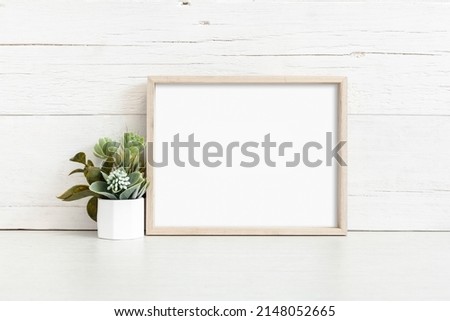 Mockup of a horizontal wooden frame on a light background. Frame 8x10 on the table with a flower.