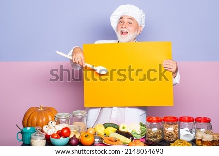 Excited senior chef in cook hat pointing spoon on blank board menu. Funny chef showing blank empty blackboard menu. Kitchen chef. Royalty-Free Stock Photo #2148054693