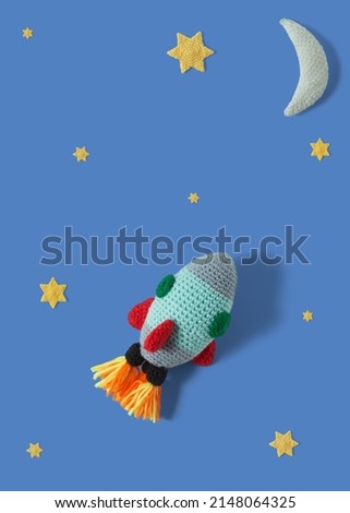Cute rocket in space, stars and moon, knitted with colored wool. Handmade crochet rocket on dark blue space background. Amigurumi rocket. Top view