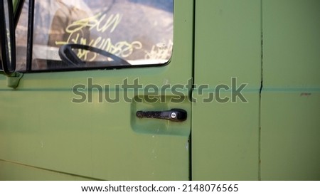 door handle in an old green car with graffiti on the glass