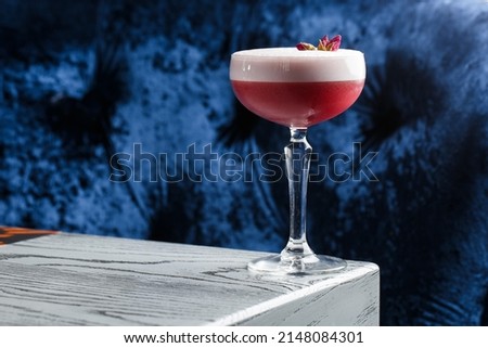 Pink Clover Club Cocktail in Coupe Glass with Layer of Foam and flower Garnish isolated on dark Background. Royalty-Free Stock Photo #2148084301