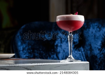 Pink Clover Club Cocktail in Coupe Glass with Layer of Foam and flower Garnish isolated on dark Background. Royalty-Free Stock Photo #2148084305