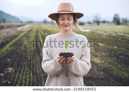 Young plant in hands in background of agricultural field area. Woman holding in hands green sprout seedling on black soil. Concept of Earth day, organic gardening, ecology, sustainable life. Royalty-Free Stock Photo #2148118455