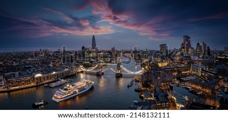 Panoramic, aerial view of the skyline of London with a motion blurred cruise ship passing under the lifted Tower Bridge during dusk, England Royalty-Free Stock Photo #2148132111