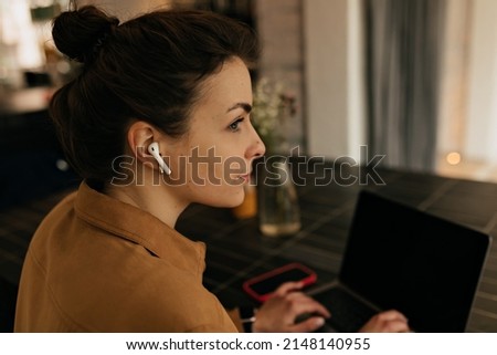 Close up portrait from back of stylish european woman with collected hair is working on laptop in stylish office and listening music in headphones. High quality photo