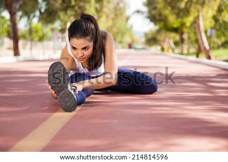 Hispanic young woman warming up and stretching at a running track outdoors