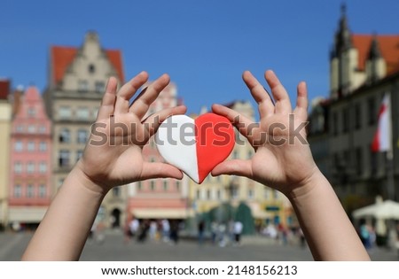 A red-white heart in the colors of the national flag of Poland in the hands of a child against the backdrop of the old town square. Independence Day of Poland. Freedom and Democracy Royalty-Free Stock Photo #2148156213