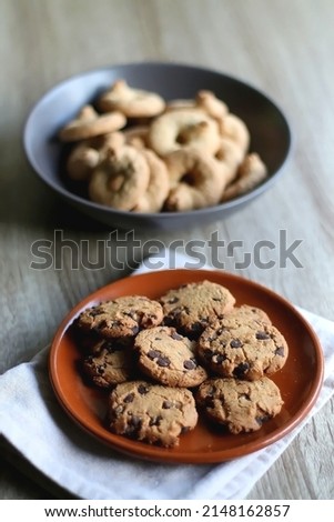 Plate of chocolate chip cookies and bowl of sugar cookies on wooden table. Selective focus.