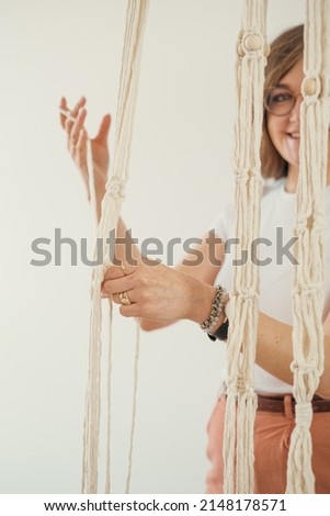 Close up of freelancer woman working on half-finished macrame piece, weaves flower pot holder. Women hobby.
