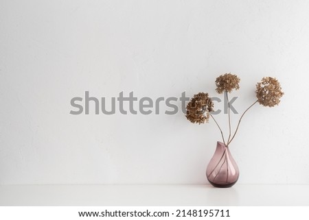Pink vase with dried branches, flowers against white wall.	
