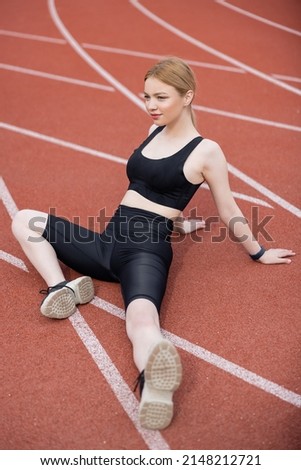 sportive woman in black sports bra and bike shorts sitting on athletic field