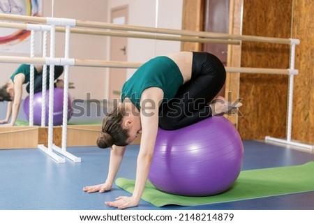 Girl in green topic do exercises with fit ball