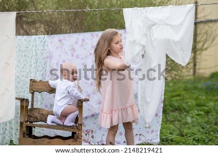 Children hang bed linen on a rope. Drying curtains and sheets on the street. Little blonde girls in the garden.