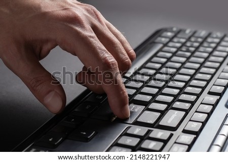 Finger presses the enter button. Typing male hands. Black keyboard button close up, English language and black light keyboard for hacker, gamer, office concept, soft focus.