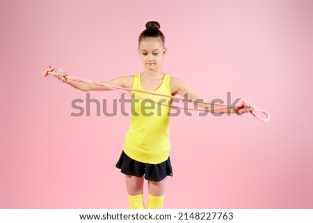 Young gymnast girl stretching and training with a skipping rope on a pink background. Sport and healthy lifestyle concept