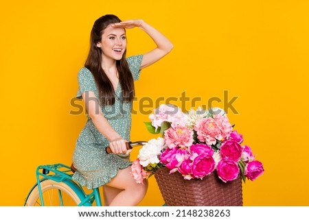 Photo of excited lady dressed green dress driving cycle pink bunch looking far away empty space isolated yellow color background