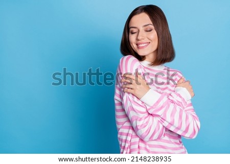 Photo of cute young brunette lady hug herself near promo wear pink pullover isolated on blue background